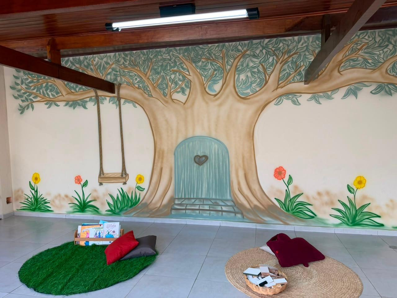 Árvore com balanço, tapete de leitura e materiais no espaço do Vila Baobá